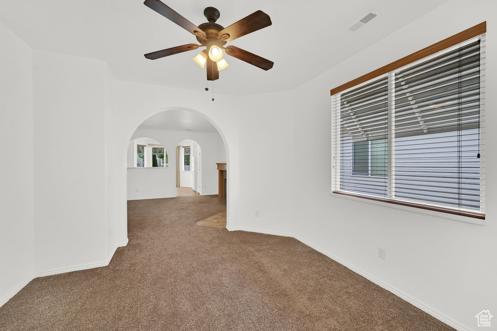 Unfurnished room featuring carpet, arched walkways, a ceiling fan, and baseboards