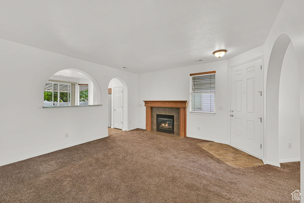 Unfurnished living room featuring carpet, healthy amount of natural light, and arched walkways