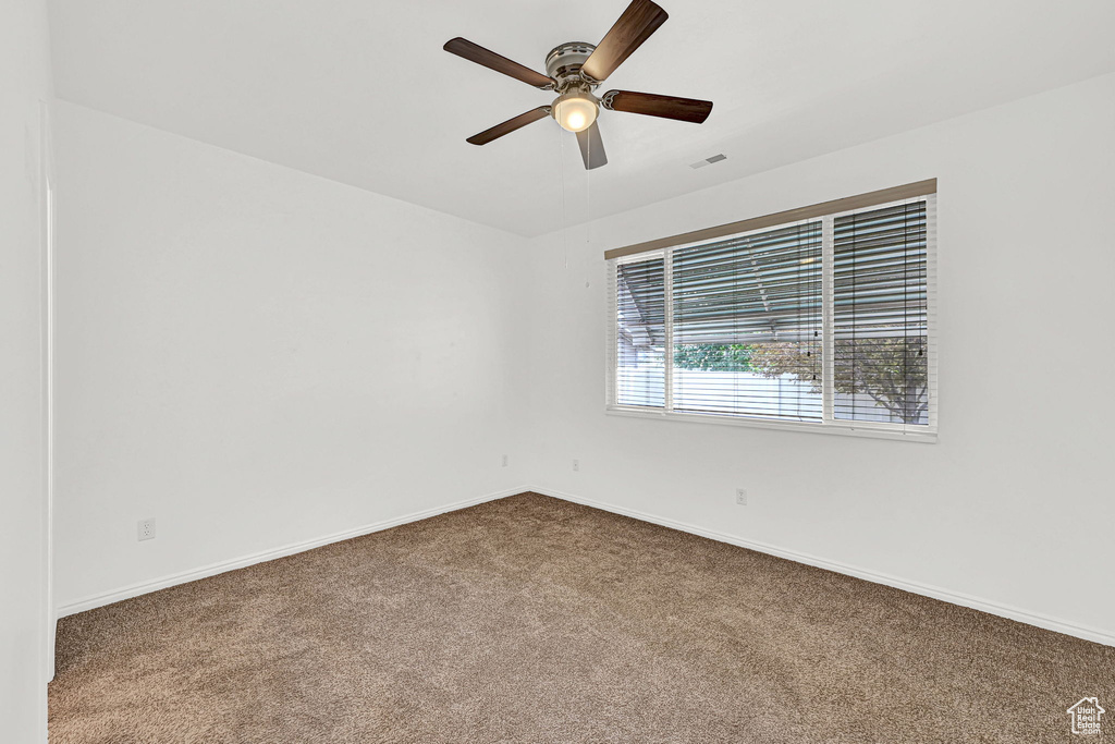 Empty room featuring dark carpet, ceiling fan, and baseboards