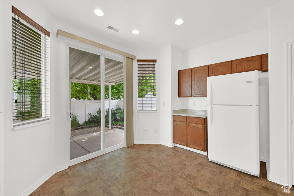 Kitchen featuring freestanding refrigerator, healthy amount of natural light, baseboards, brown cabinetry, and recessed lighting