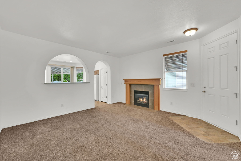 Unfurnished living room featuring carpet, baseboards, a fireplace, and arched walkways