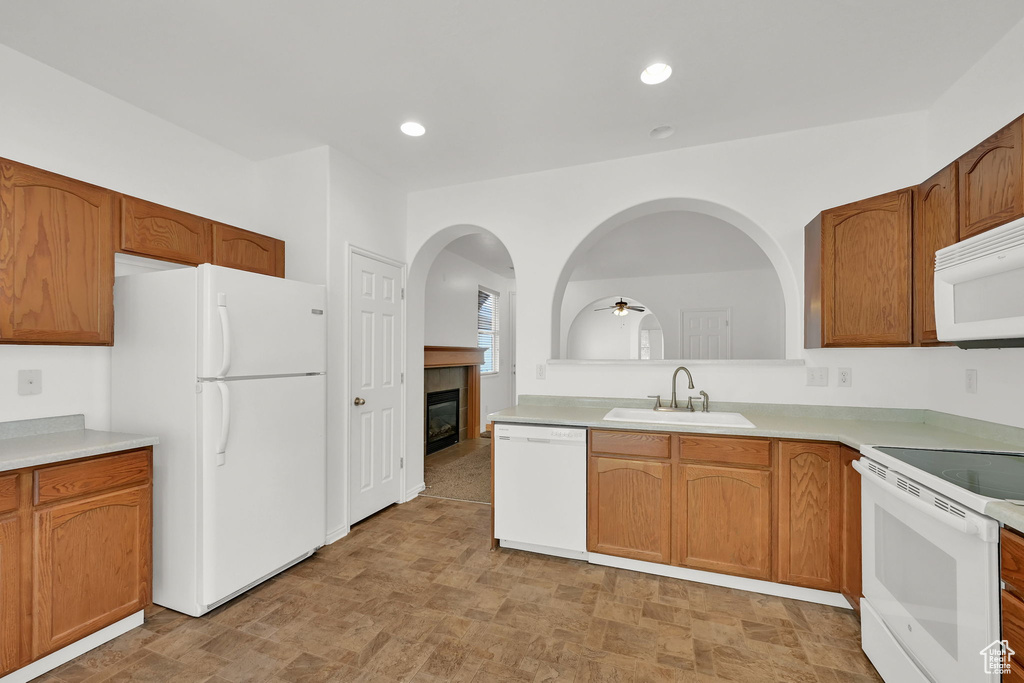 Kitchen with white appliances, a sink, a glass covered fireplace, light countertops, and a ceiling fan
