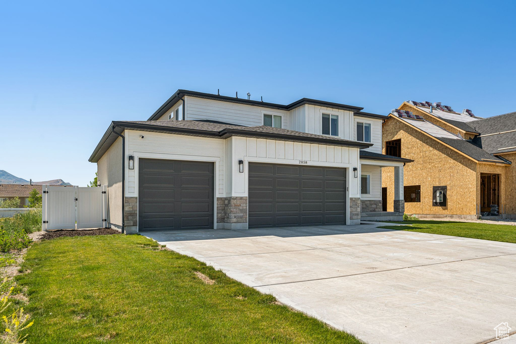 View of front of house featuring an attached garage, a gate, concrete driveway, board and batten siding, and stone siding