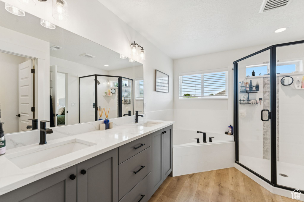 Full bathroom featuring a bath, a stall shower, double vanity, and wood finished floors