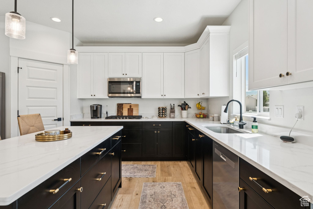 Kitchen featuring appliances with stainless steel finishes, dark cabinetry, a sink, white cabinets, and light wood-type flooring