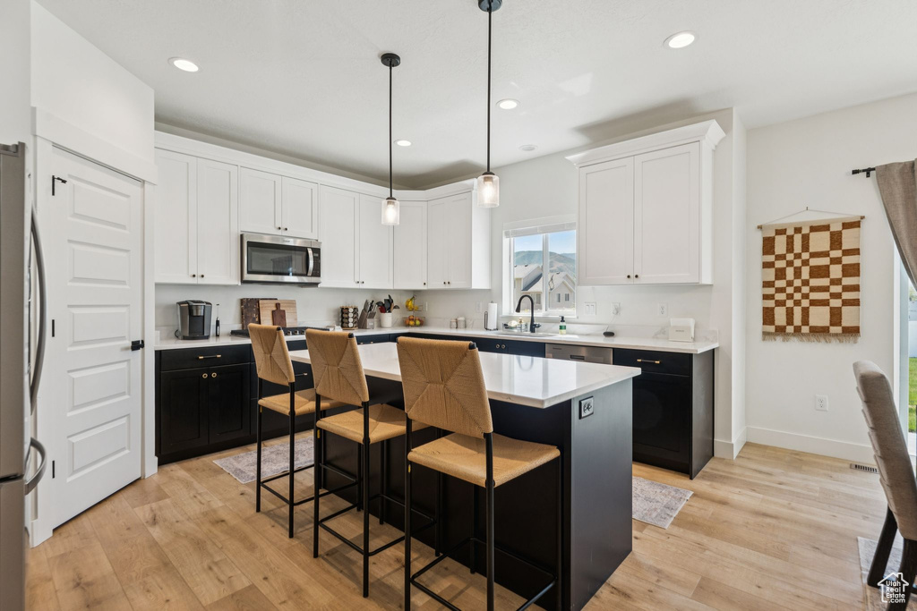 Kitchen featuring stainless steel appliances, white cabinetry, a breakfast bar, light countertops, and a kitchen island