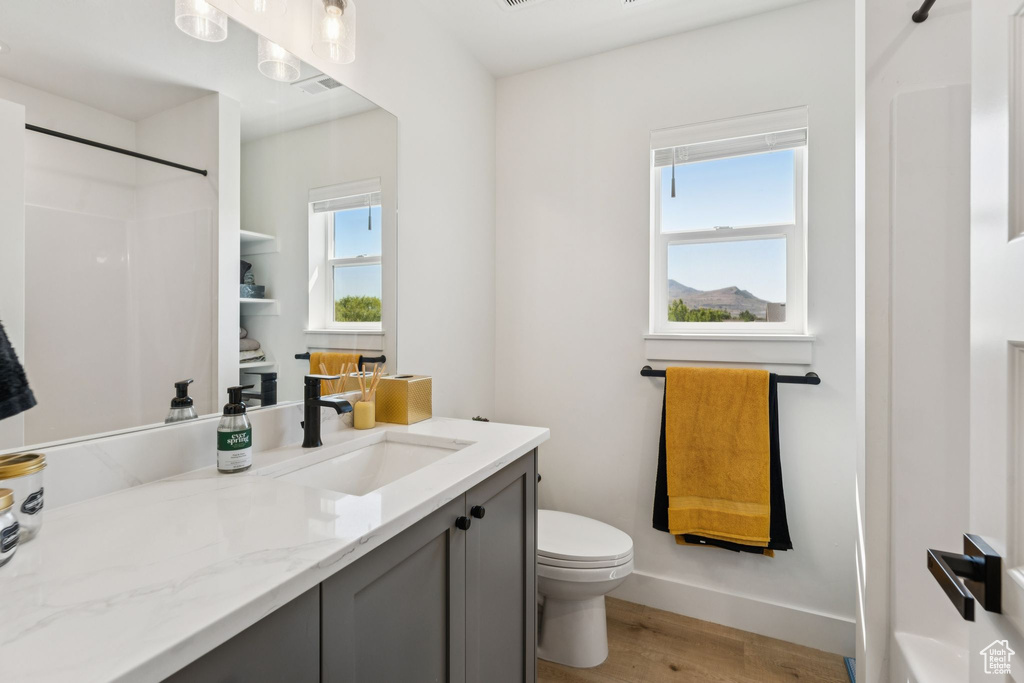 Bathroom featuring vanity, wood finished floors, toilet, a shower, and baseboards