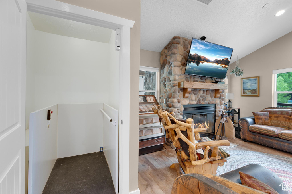 Living room featuring lofted ceiling, light wood-style floors, and a stone fireplace