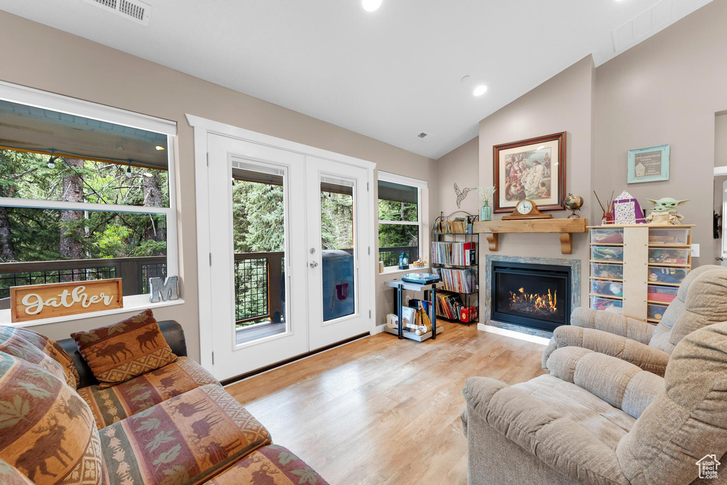 Living area with vaulted ceiling, wood finished floors, a warm lit fireplace, recessed lighting, and french doors
