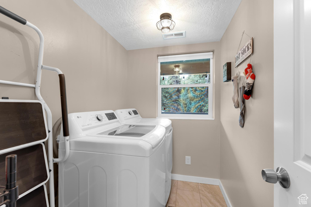Washroom featuring independent washer and dryer, a textured ceiling, baseboards, and light tile patterned floors