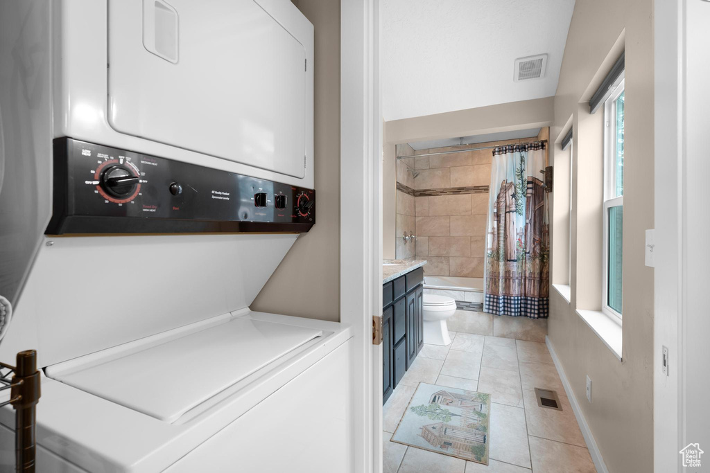 Laundry area with stacked washer / drying machine and light tile patterned flooring