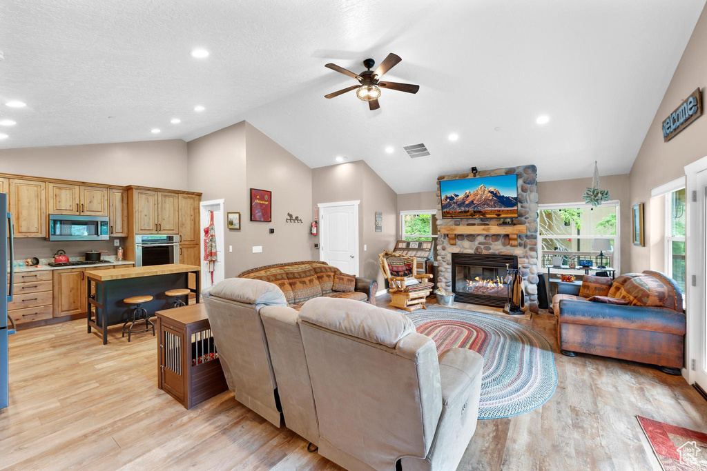 Living room with a ceiling fan, light wood-type flooring, a stone fireplace, high vaulted ceiling, and recessed lighting