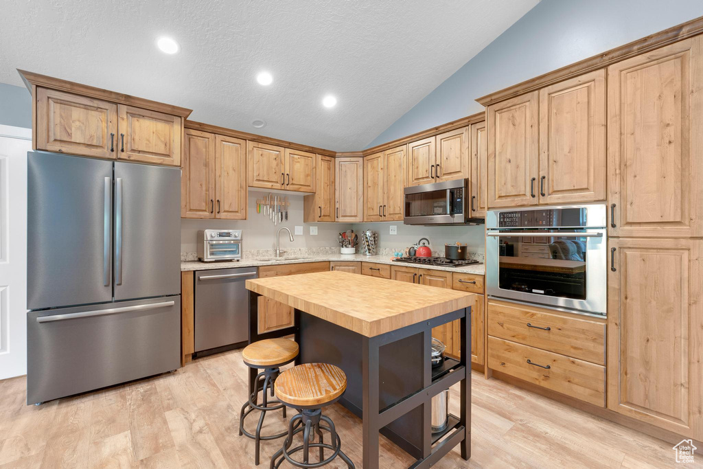 Kitchen with appliances with stainless steel finishes, a sink, butcher block counters, lofted ceiling, and light wood-style floors