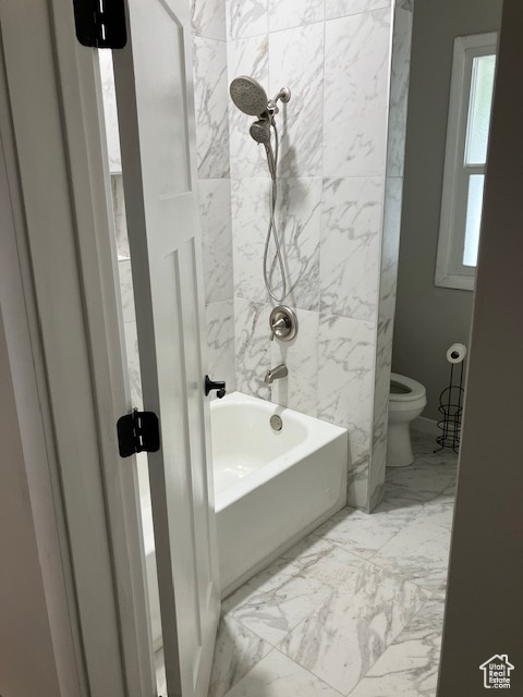 Full bath featuring toilet, marble look tiles, and shower / tub combination