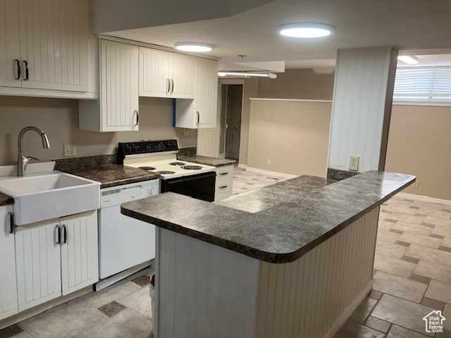 Kitchen featuring dishwasher, electric range, a sink, dark countertops, and a peninsula