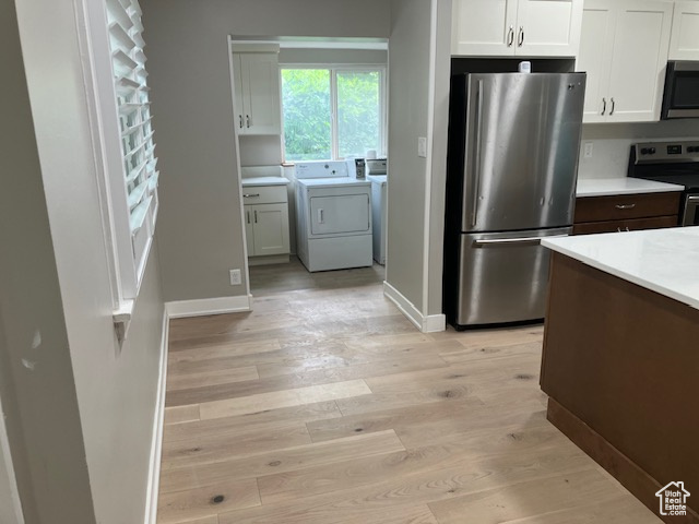 Kitchen with stainless steel appliances, light wood-type flooring, washer and clothes dryer, light countertops, and white cabinets