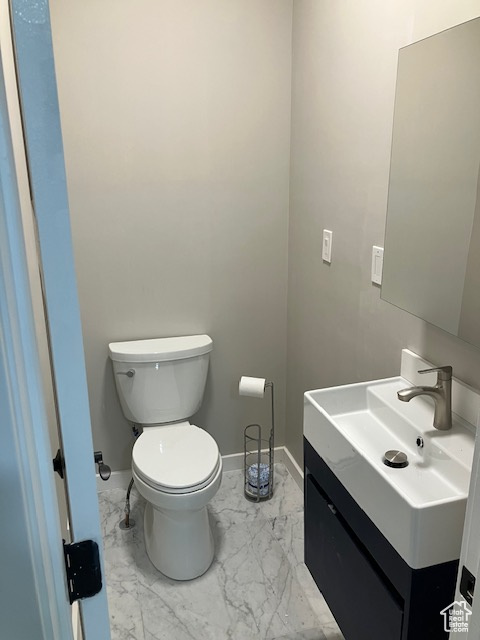 Bathroom with toilet, vanity, marble finish flooring, and baseboards