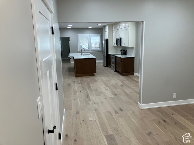 Kitchen featuring stainless steel appliances, a sink, baseboards, a center island with sink, and light wood finished floors