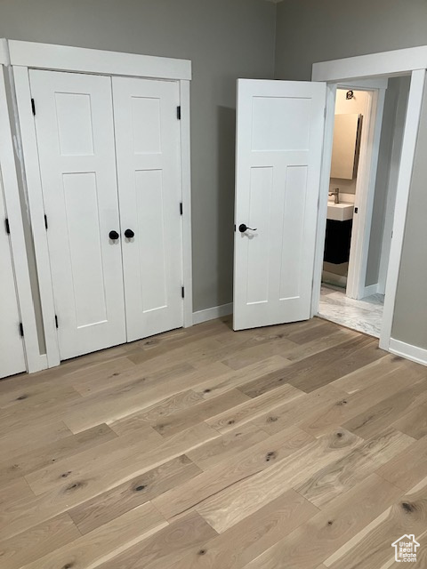 Unfurnished bedroom featuring light wood-style floors, baseboards, a sink, ensuite bathroom, and a closet