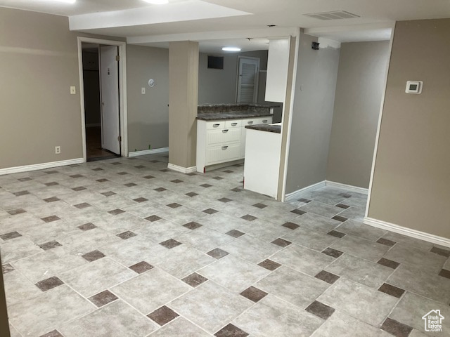 Kitchen with dark countertops, baseboards, and white cabinetry