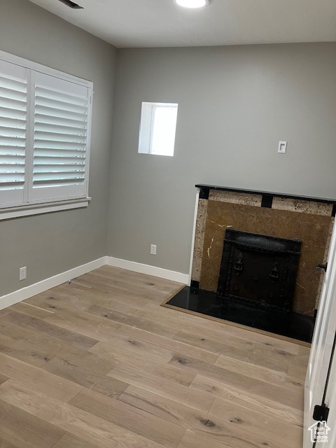 Unfurnished living room with light wood finished floors, a high end fireplace, and baseboards