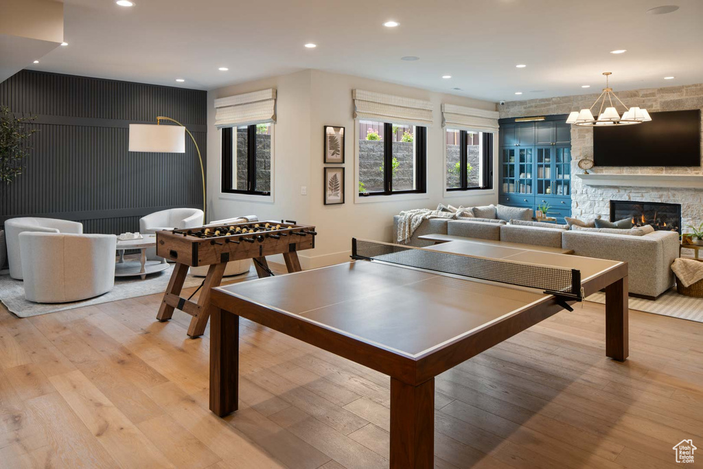 Rec room featuring light wood-style floors, a stone fireplace, recessed lighting, an accent wall, and a chandelier