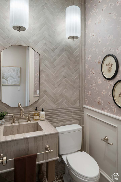 Bathroom featuring toilet, vanity, wainscoting, and wallpapered walls
