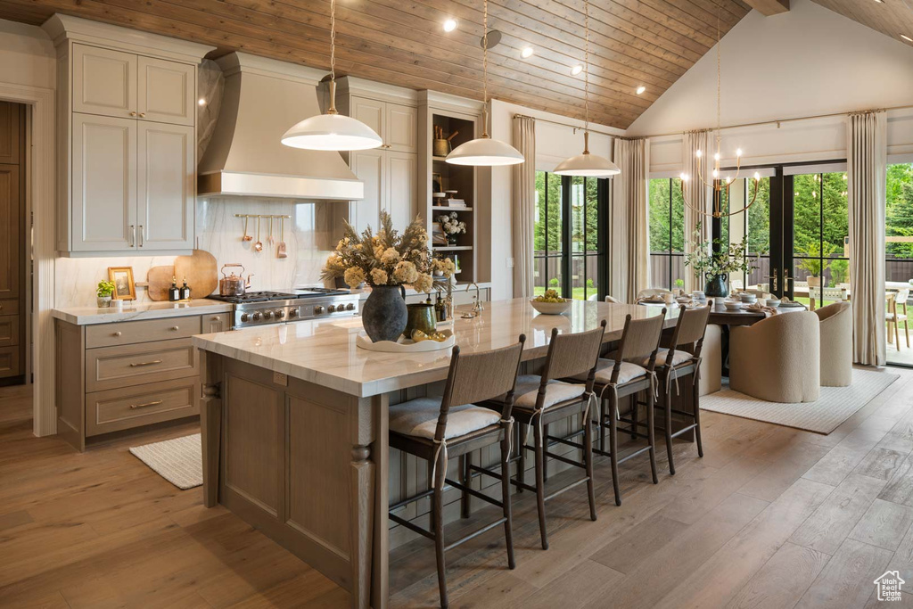 Kitchen featuring premium range hood, wooden ceiling with exposed beams, light wood-type flooring, a kitchen island with sink, and range