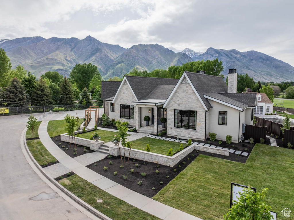 View of front of house with a chimney, stone siding, a mountain view, a shingled roof, and stucco siding
