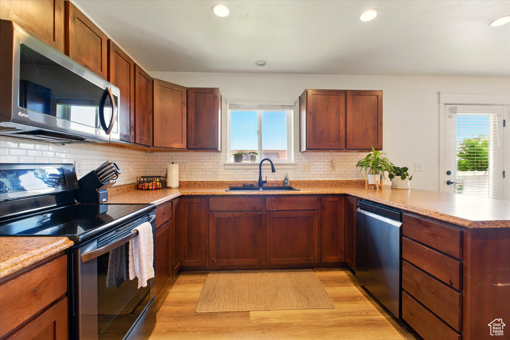 Kitchen with stainless steel appliances, a sink, light wood-style floors, a peninsula, and recessed lighting