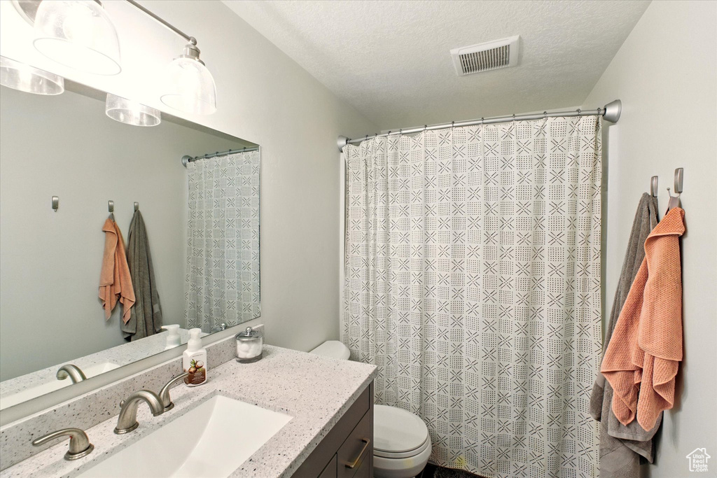 Bathroom featuring toilet, vanity, a textured ceiling, and a shower with curtain