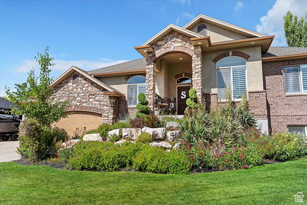 View of front facade featuring stucco siding, a front yard, a garage, and stone siding