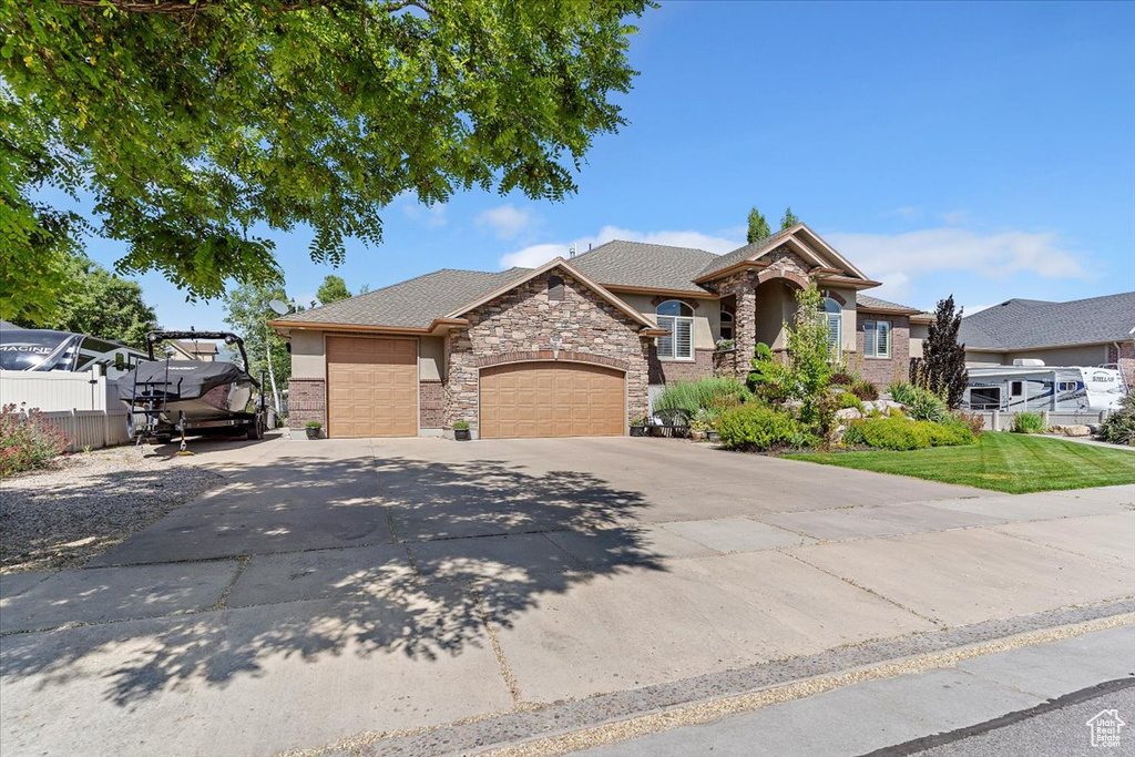 View of front facade featuring a garage, stone siding, concrete driveway, and stucco siding