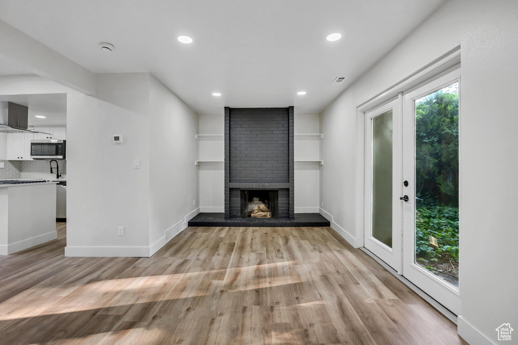 Unfurnished living room with light wood finished floors, baseboards, recessed lighting, a brick fireplace, and a sink