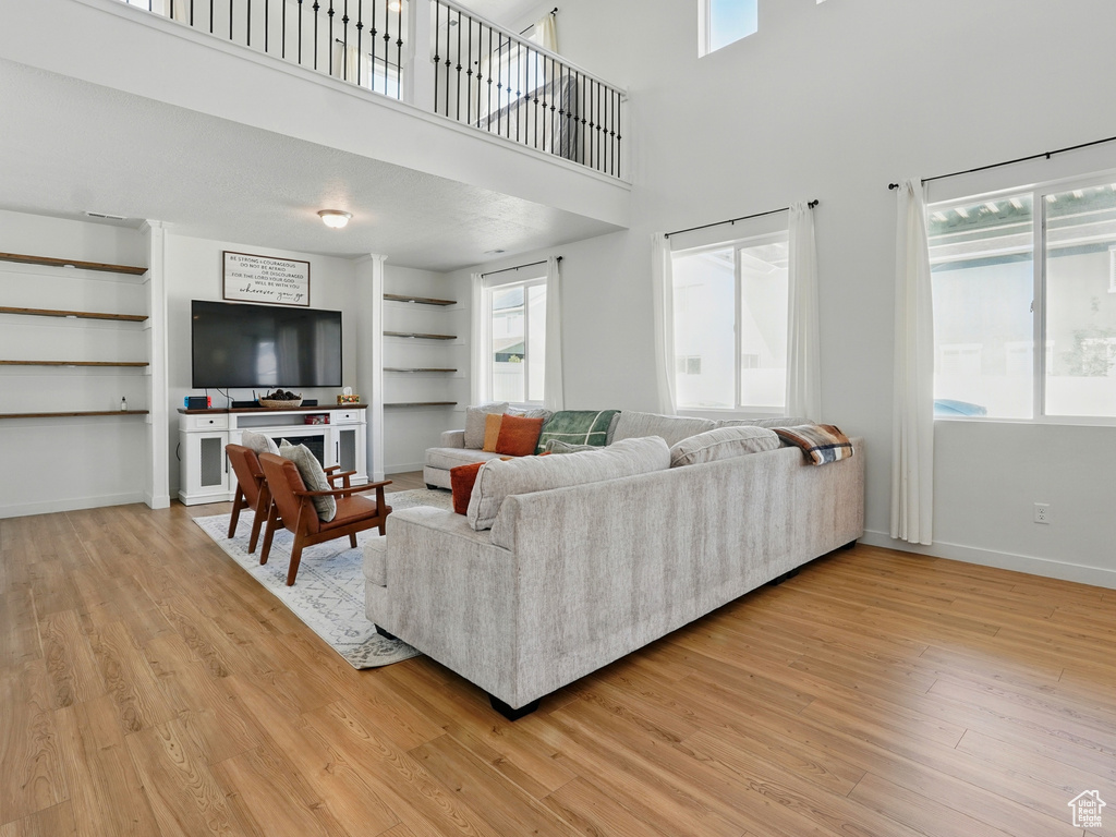 Living area with light wood-style flooring, built in shelves, baseboards, and a towering ceiling