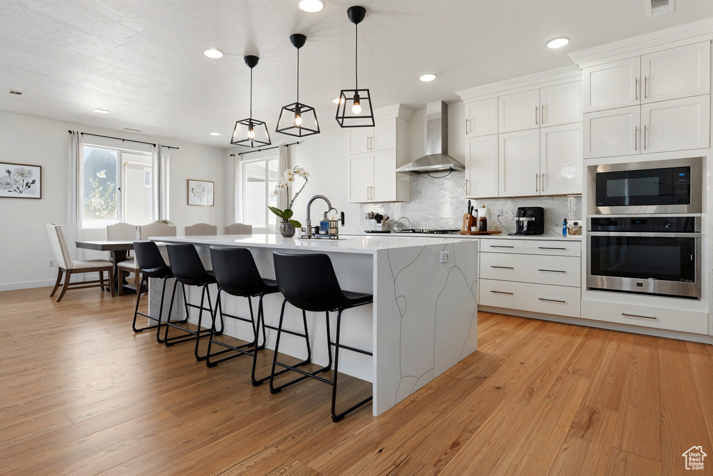 Kitchen with oven, wall chimney range hood, built in microwave, a kitchen bar, and tasteful backsplash