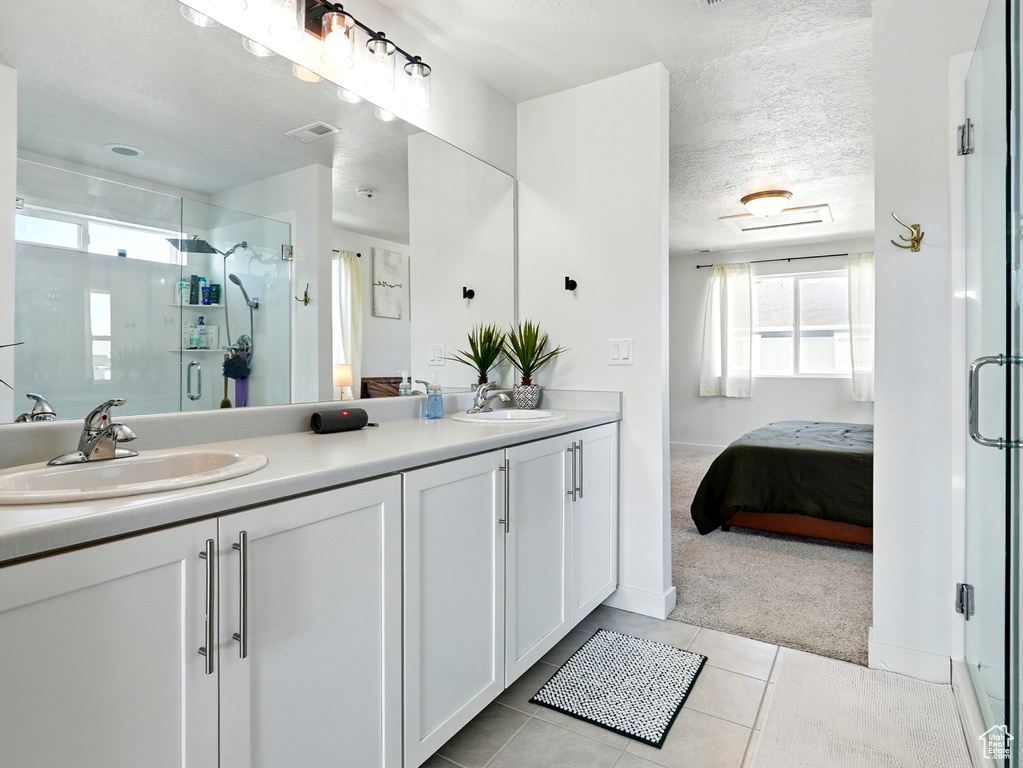 Full bath with double vanity, tile patterned floors, ensuite bathroom, a stall shower, and a textured ceiling