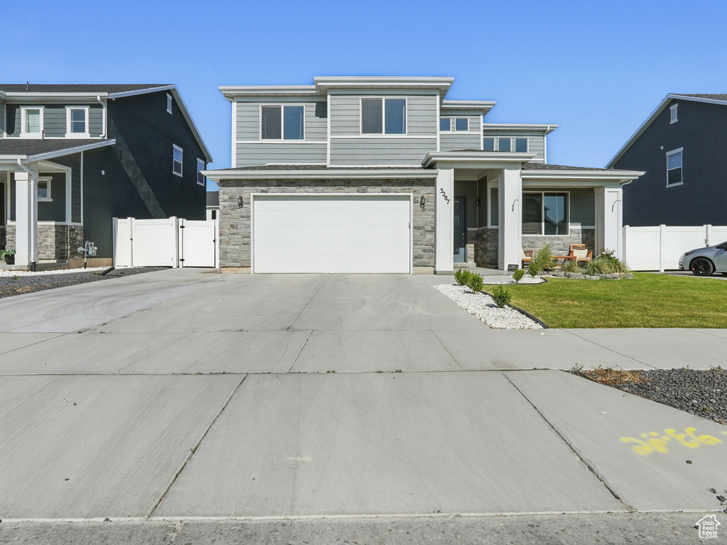 View of front of home featuring stone siding, driveway, an attached garage, a gate, and covered porch