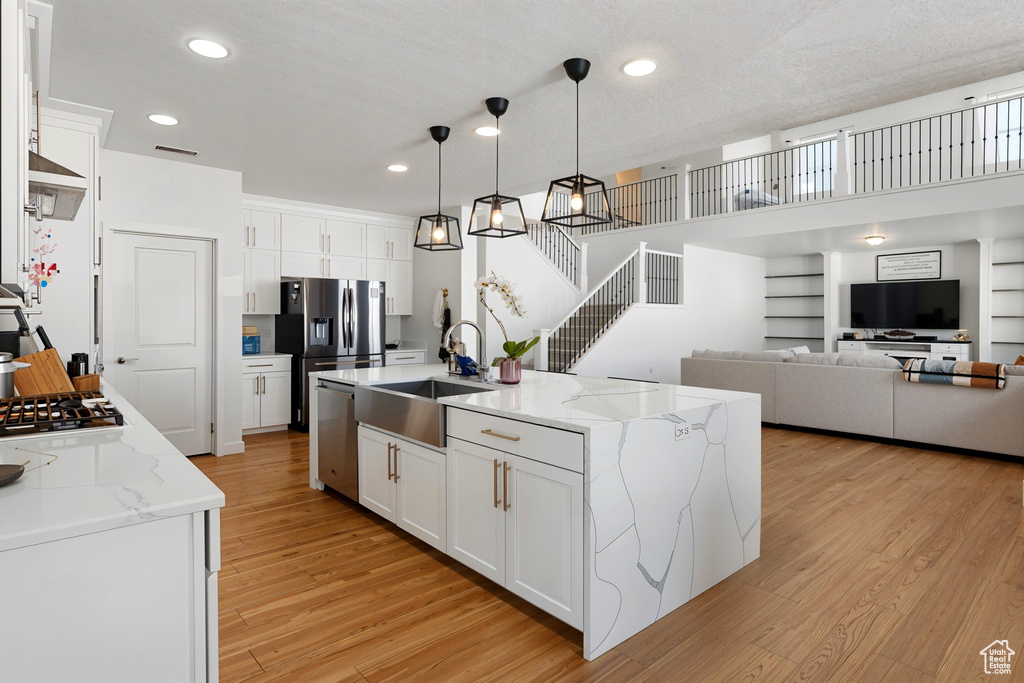 Kitchen featuring a sink, stainless steel appliances, light wood finished floors, white cabinets, and pendant lighting