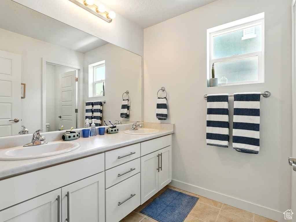 Bathroom featuring double vanity, toilet, baseboards, and tile patterned floors