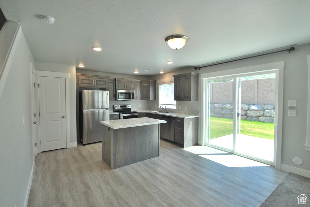 Kitchen featuring stainless steel appliances, a kitchen island, light countertops, light wood-style floors, and baseboards