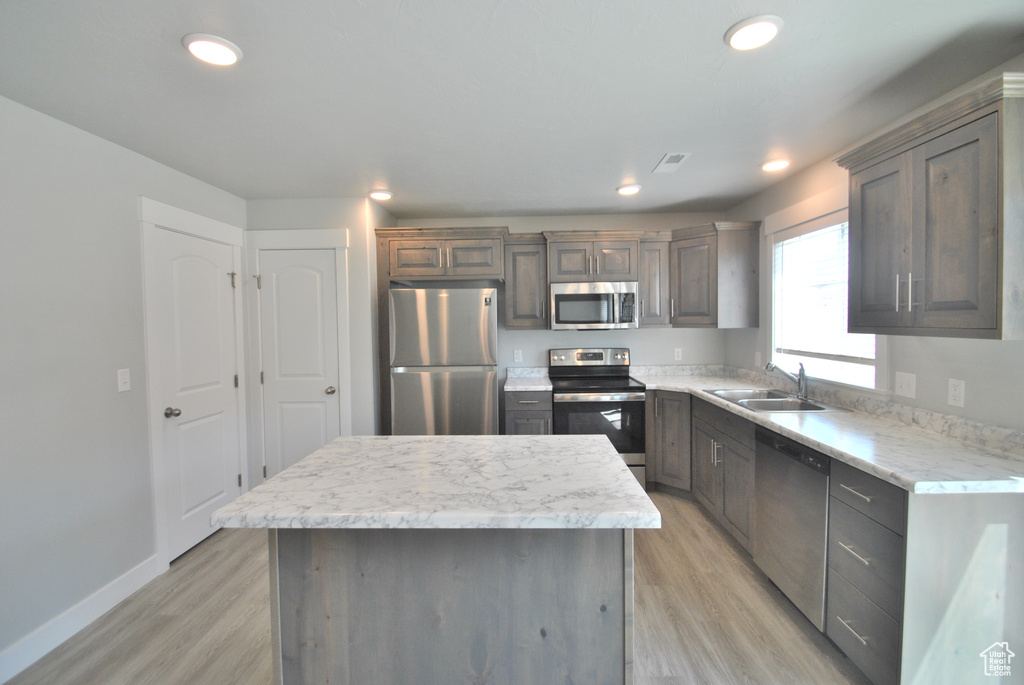 Kitchen with stainless steel appliances, a sink, light wood finished floors, a center island, and recessed lighting