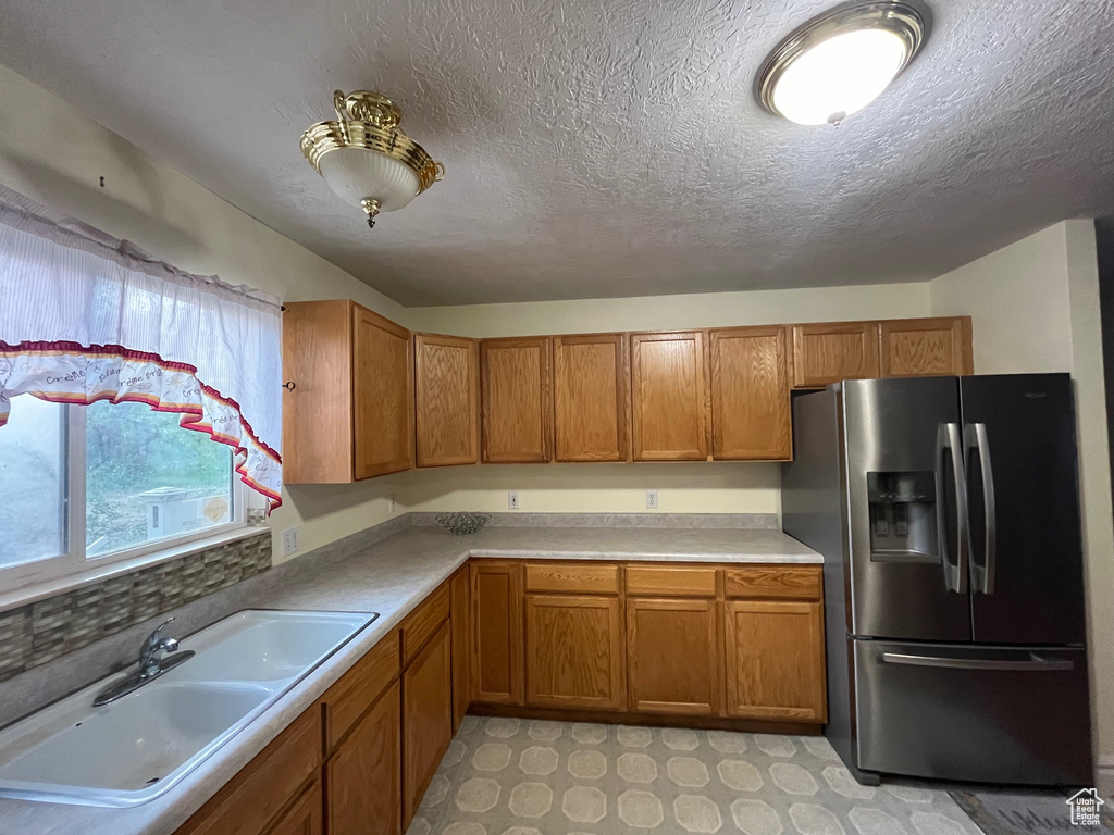 Kitchen featuring stainless steel fridge, a sink, brown cabinetry, light countertops, and a textured ceiling