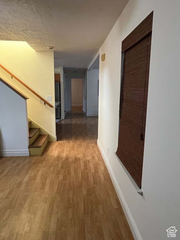 Corridor with light wood-style floors, baseboards, stairs, and a textured ceiling