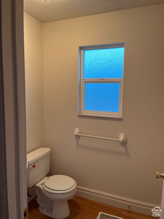 Bathroom featuring toilet, wood finished floors, baseboards, and a textured ceiling