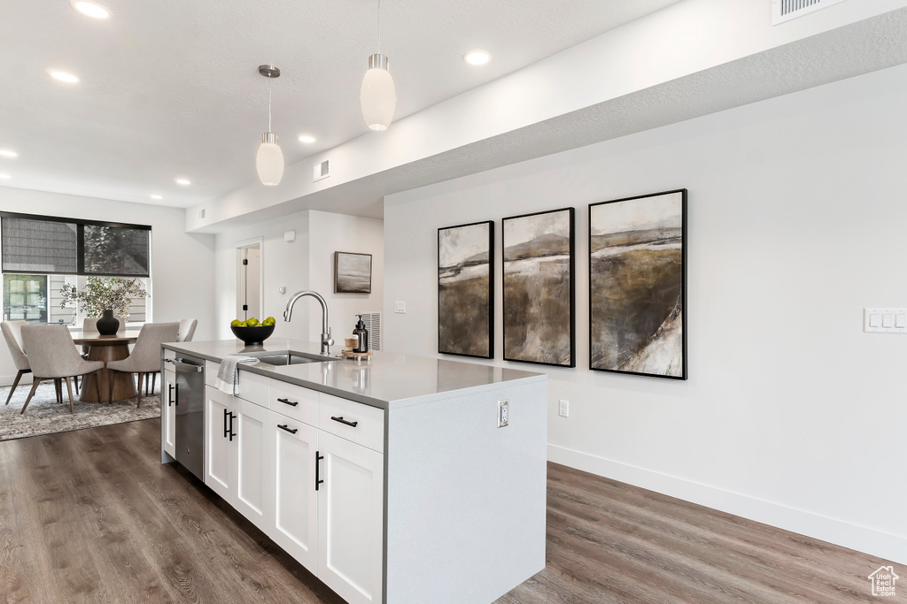 Kitchen featuring a sink, dark wood-type flooring, an island with sink, white cabinetry, and decorative light fixtures