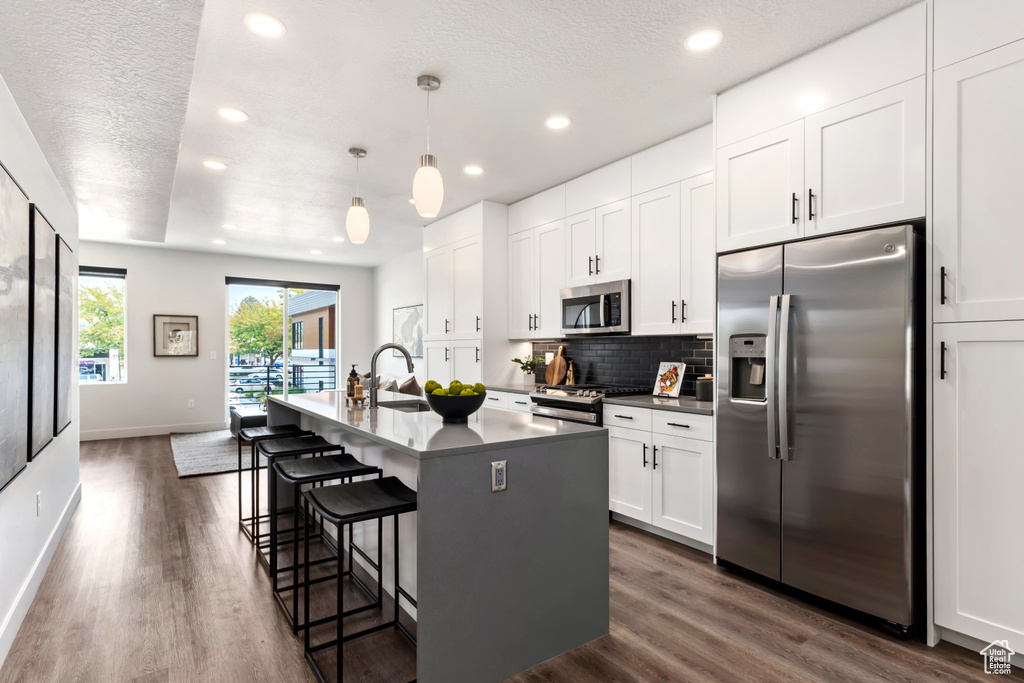 Kitchen with appliances with stainless steel finishes, recessed lighting, backsplash, white cabinetry, and a center island with sink