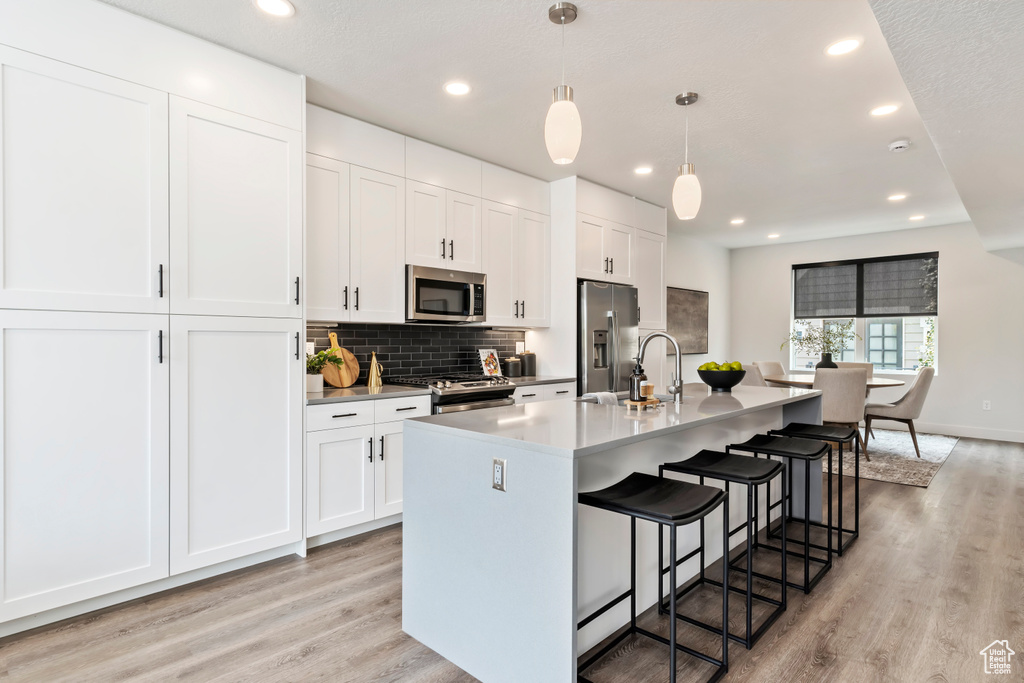 Kitchen with appliances with stainless steel finishes, a kitchen island with sink, light wood-style flooring, a breakfast bar, and recessed lighting
