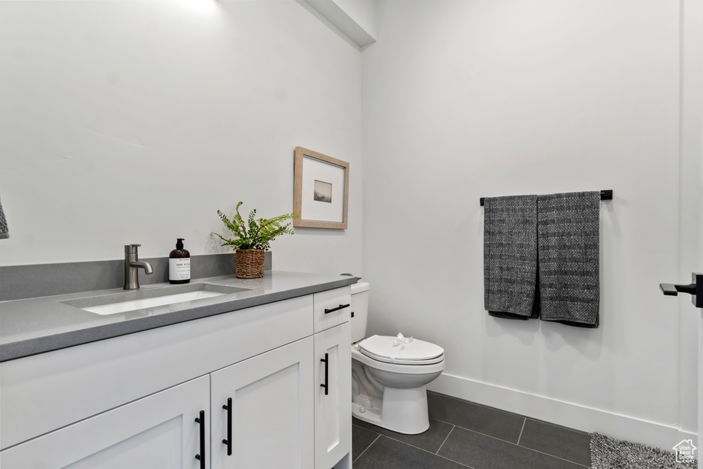 Half bath featuring tile patterned floors, vanity, toilet, and baseboards