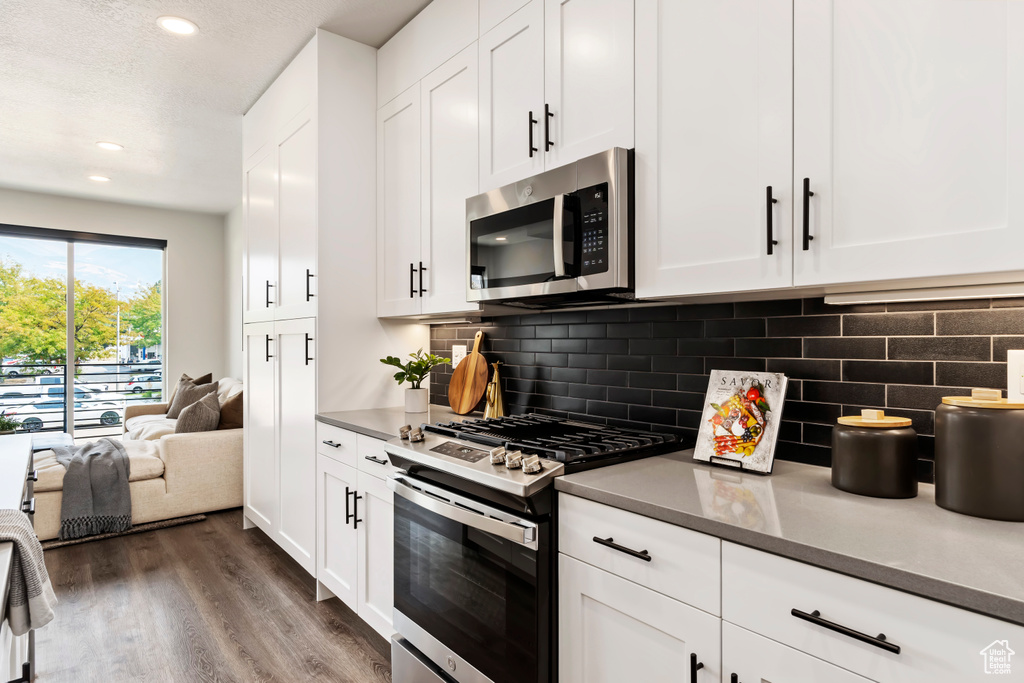 Kitchen with appliances with stainless steel finishes, dark wood-style floors, backsplash, white cabinetry, and recessed lighting